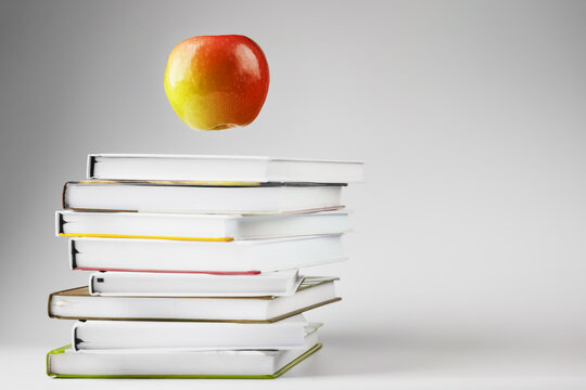 A red Apple hovers over a stack of books on a light background.