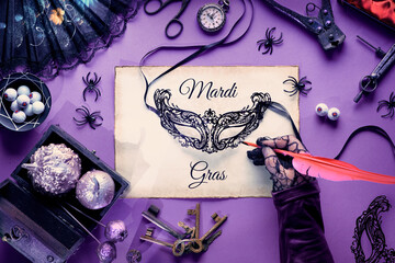 Creative Halloween or Mardi Gras background in purple, white and black. Text Mardi Gras on parchment. Carnival mask, fan, vintage keys, hand glove with quill. Creative flat lay for masquerade