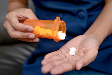 Close up of working woman taking in pill she is pours the pills out of the bottle,taking painkiller to reduce sharp ache concept,health care and medicine concept.