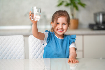 Cute little girl drinking water in kitchen at home. Prevention of dehydration