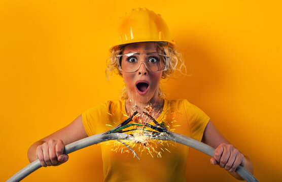 Worker girl with hat breaks an electric cable. Yellow background