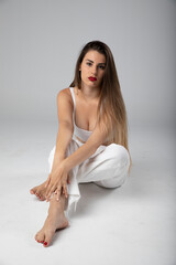 Fototapeta premium Modelo joven sentada sobre fondo blanco y ropa blanca con pelo largo