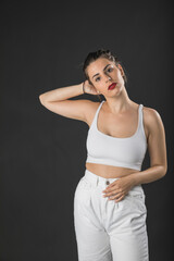 Modelo mujer joven de pelo largo posando con top blanco y pantal&oacute;n blanco sobre fondo negro.