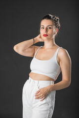 Modelo mujer joven de pelo largo posando con top blanco y pantalón blanco sobre fondo negro.