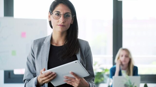 Video of a young smart business woman using her digital tablet and then looks at the camera and take off the glasses in the coworking space.