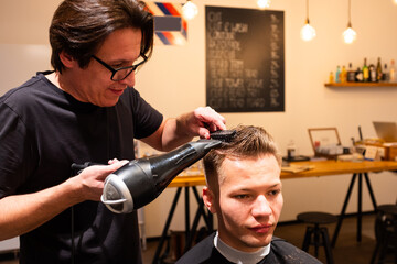 Barber dries the hair of man with hairdryer and brush