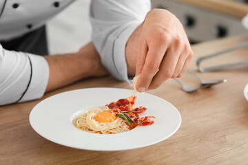 Obraz na płótnie Canvas Male chef cooking tasty pasta carbonara in kitchen, closeup