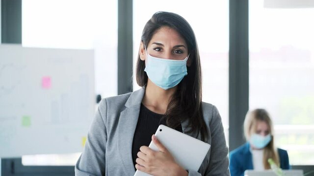 Video of pretty business woman wearing a hygienic face mask while work with her digital tablet in the coworking space.