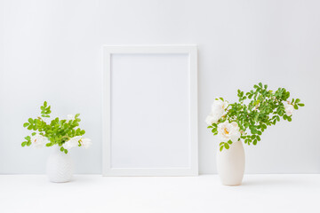 Home interior with decor elements. Mockup with a white frame and small flowers and green leaves in a vase on a light background
