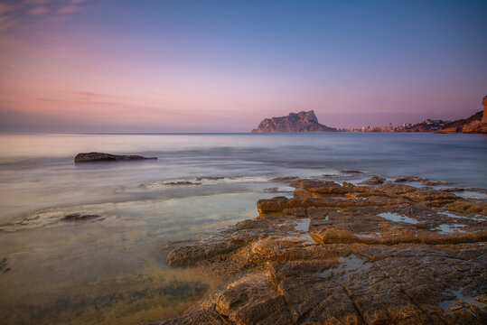 Paisaje de costa de la cala baladrar, en el mar mediterr&aacute;neo, atardecer dentro del agua, y el pe&ntilde;&oacute;n de Ifach de Calpe en el fondo del encuadre.