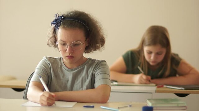 Close portrait of schoolgirls teenage girls. They sit at their desks in the classroom and write in notebooks. Class dictation