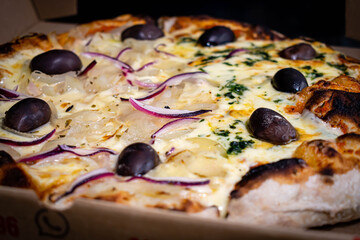 primer plano de pizza a la piedra entera con queso caliente aceitunas negras cebolla sobre madera con fondo oscuro 