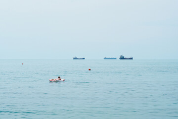 Girl sunbathes on an inflatable raft in the sea, ships in the background, sea horizon
