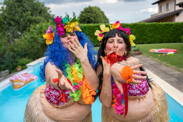 two smiling female friends dressed in Hawaiian costumes are kissing