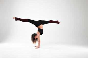 Fototapeta premium Girl in a gymnastic handstand in twine on a white background. Gymnastics, rhythmic gymnastics, practice, workout, strength, flexibility, stretching, performance.