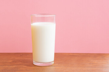 Glass of fresh milk on wooden table with pink background with copy space. Single object