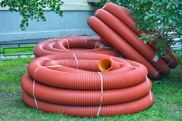 Coils of new red plastic pipe with rain drops on city lawn with green grass