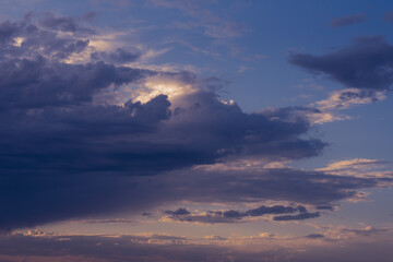 Dramatic rainy clouds on purple evening sky. Natural background with stormclouds and sunlights of setting sun.