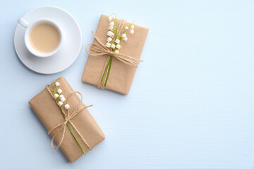 Morning cup of coffee and gift boxes on decorated lily of the valley flowers on blue table top view. Beautiful breakfast. Flat lay style