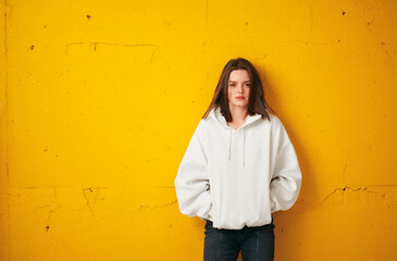 Portrait of a young pretty female student in a white hoodie, casual clothing against a concrete orange wall.