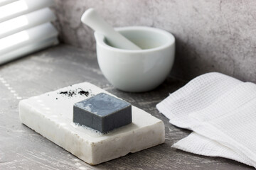 Handmade soap with activated carbon on marble, carbon powder and a cotton towel on a gray background.