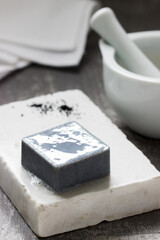 Handmade soap with activated carbon on marble, carbon powder and a cotton towel on a gray background.