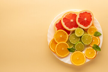 slices of grapefruit, orange, lime on a plate on a yellow surface top view