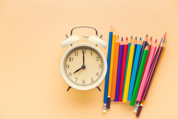 White alarm clock and color pencils on a yellow background