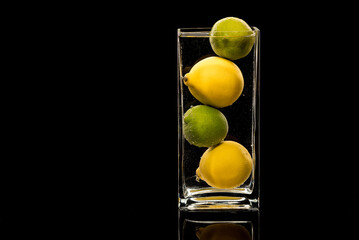 Lemon, lime in a glass vase on a black background in water