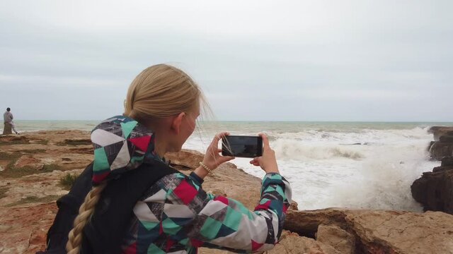 A steady shot of Girl stands with her back and takes a photo on her cell phone the sea. Slow motion