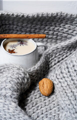 A mug of milk spicy tea, cinnamon stick and star anise. Gray knitted scarf as a background 