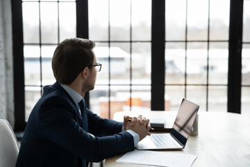 Thoughtful successful businessman look in window distance planning or pondering about business startup, pensive male boss or CEO in suit lost in thoughts thinking considering, make solution