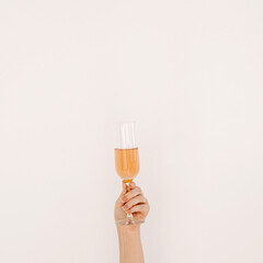 Cheers! Women's hand holding glass of rose champagne against white wall. Happy Birthday, anniversary party celebrating decoration festive concept