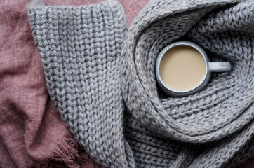 A mug of tea with milk, gray chunky knit scarf around the cup. 