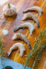 Raw shrimps on the wooden board with salt, dry pepper and rosemary