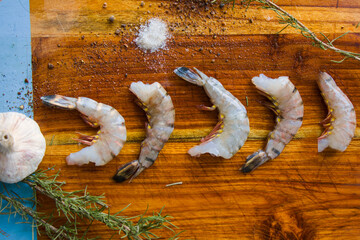 Raw shrimps on the wooden board with salt, dry pepper and rosemary