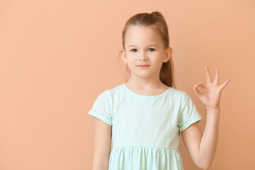 Cute little girl showing OK on color background