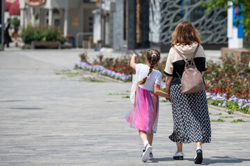 mom and daughter are walking around the city holding hands. back girl and woman in skirts on a spring day
