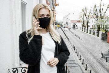 Fototapeta premium A girl in a black mask is standing on the balcony of the office and talking on the phone