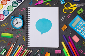 Expressing opinion concept. Top above overhead view photo of colorful pens and pencils around blank notebook with blue bubble sticker isolated on blackboard