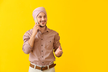 Handsome young Indian man talking by mobile phone on color background