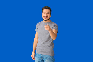 Handsome young man pointing at viewer on color background