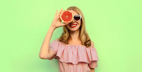 Summer portrait of smiling young woman showing juicy grapefruit over green background