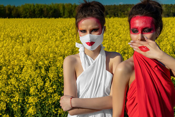 Two beautiful young brunette girls with creative bright makeup in tunics against a blue sky in a mask