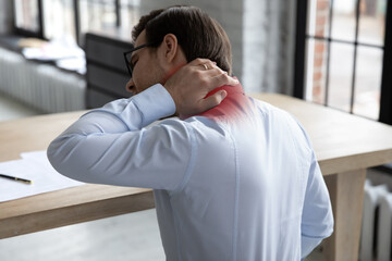 Rear view of unwell businessman touch massage neck suffer from muscular spasm or strain, unhealthy male employee struggle with backache, sit in incorrect posture, sedentary lifestyle concept