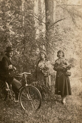 Fototapeta na wymiar Germany - CIRCA 1930s: Man on bicycle talking with two woman in forest. Vintage archive Art deco era photo