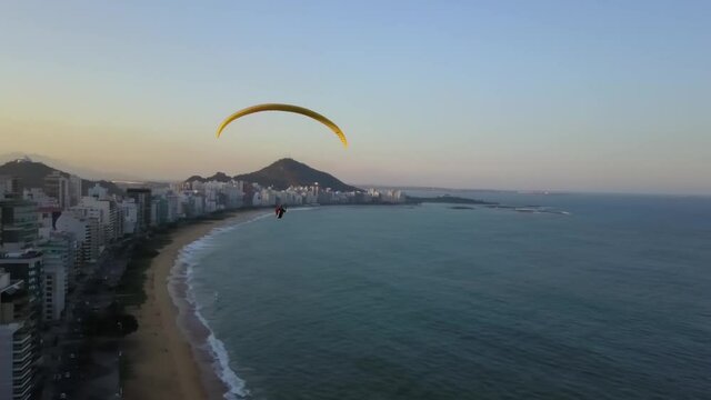 Yellow paraglider flying in Praia da Costa, Esp&iacute;rito Santo, Brazil. Parapente na Praia da Costa, Brasil. Flying below drone shot.