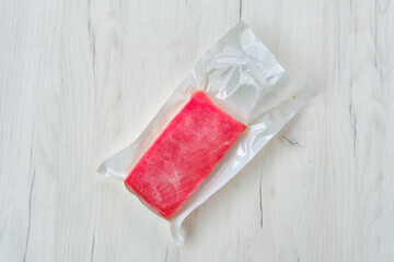 Raw frozen tuna fillet in vacuum packaging on wooden background