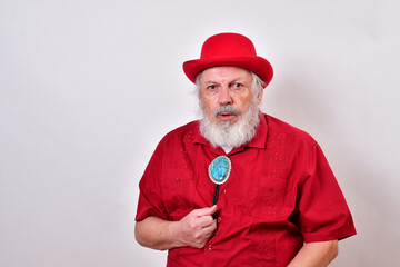 Well dressed old man wearing a red derby hat, red shirt and large bolo tie reacting to a chest pain...