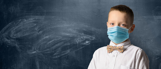School boy wearing face mask standing against blackboard. Safe back to school during pandemic...